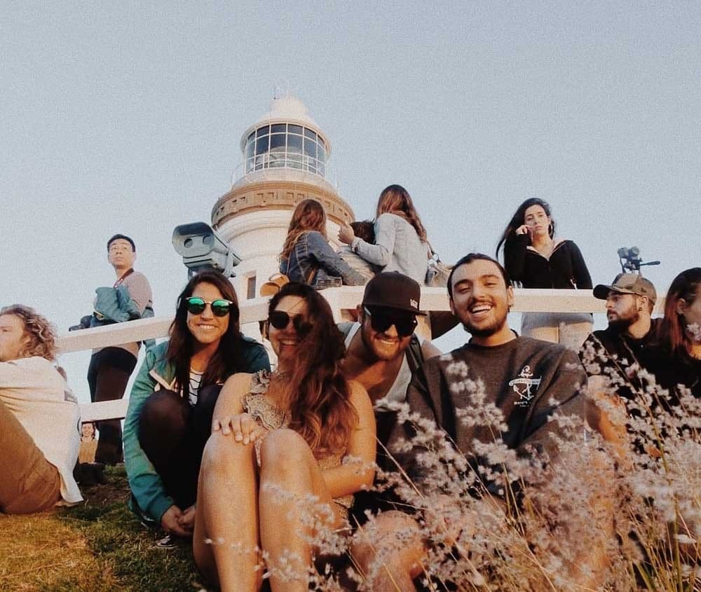 grupo de amigos sonriendo y mirando a cámara y detrás el Faro de Byron Bay